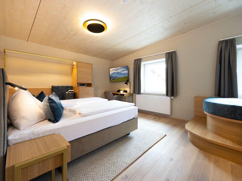 Hell eingerichtetes Hotelzimmer mit Doppelbett und Whirlpool neben dem Fenster.