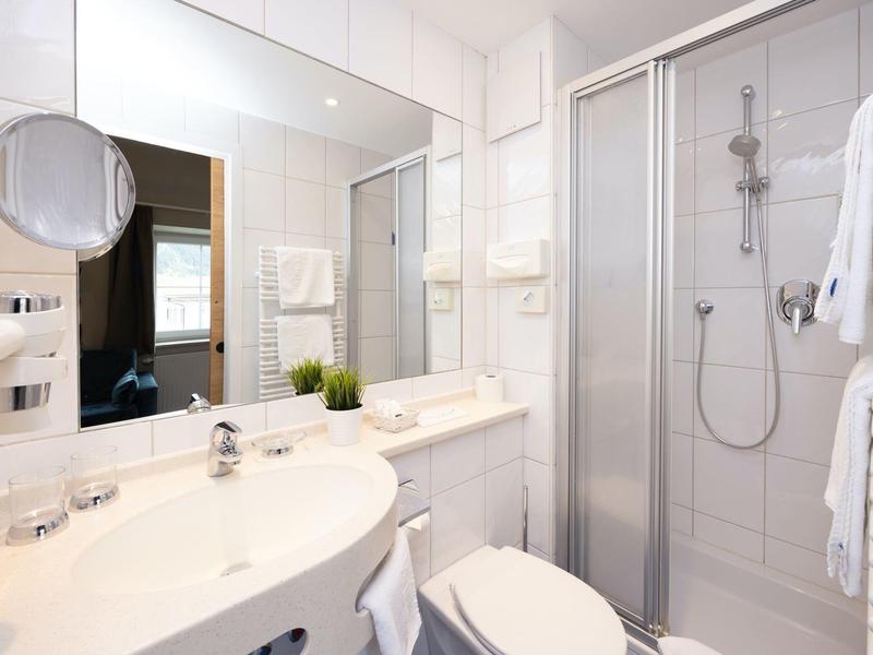 Modernes, weiß gefliestes Badezimmer mit Dusche, Toilette und großem Spiegel.