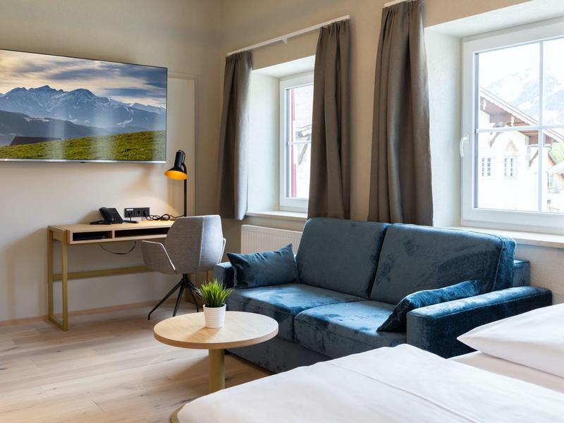 Modernes Hotelzimmer mit blauem Sofa, Schreibtisch, großem Fenster und Doppelbett.