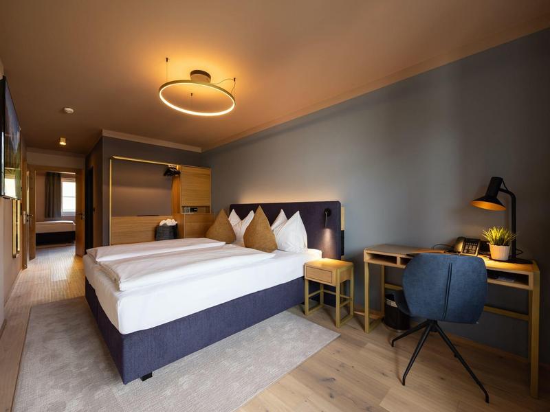 Modern eingerichtetes Hotelzimmer mit Doppelbett, Schreibtisch und Stuhl in gedeckten Farben.