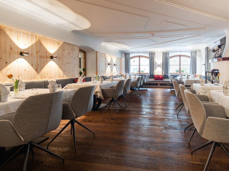 Eleganter Speisesaal mit hellen Stühlen und Holzboden, großer Fensterfront im Hintergrund.