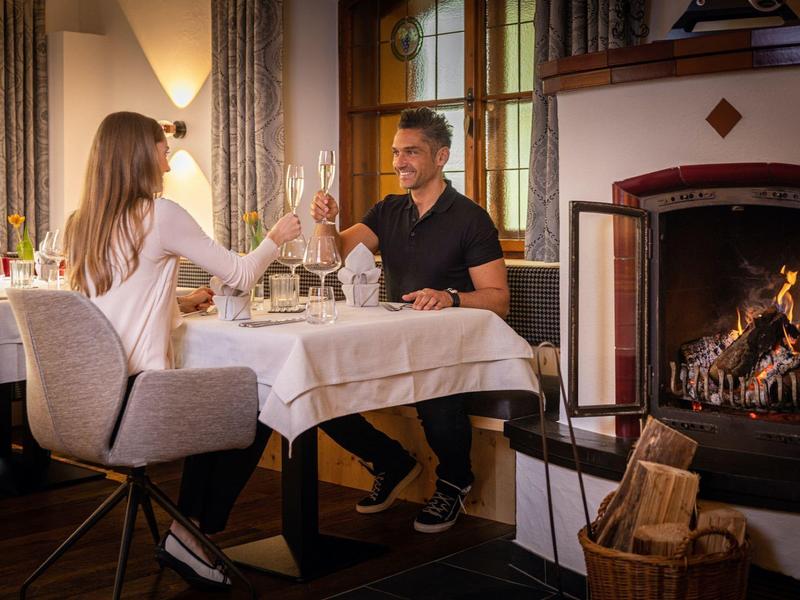 Paar stößt beim Abendessen am Tisch vor einem Kamin an.