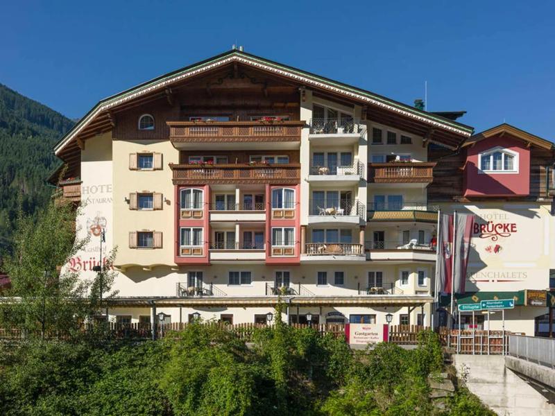Mehrstöckiges Hotel im Alpenstil mit Balkonen und grünem Buschwerk im Vordergrund