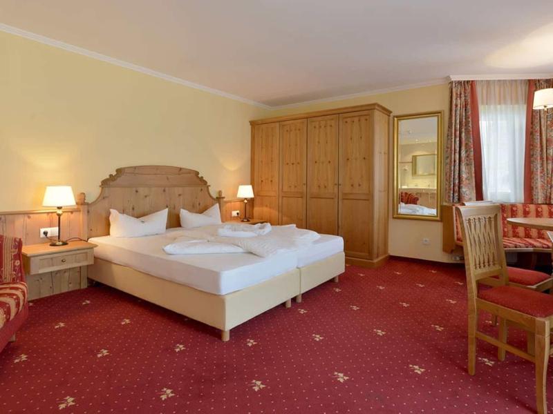 Gemütliches Hotelzimmer mit Doppelbett, Holzmöbeln und rotem Teppichboden.