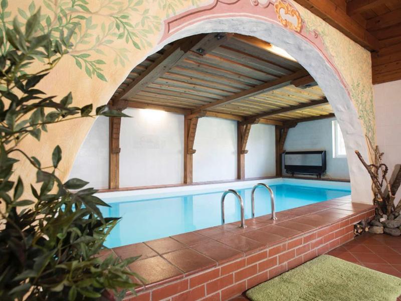 A covered indoor pool with wooden beams and plant in a wood-paneled room.