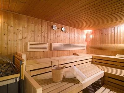 Holzsauna mit hellen Holzliegen, Thermometern an der Wand und einem Holzeimer mit Kelle.