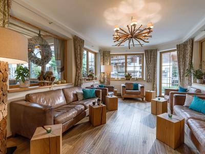 Przytulny salon z brązową skórzaną sofą, fotelami i nowoczesnym żyrandolem.