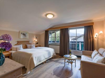 Jasny pokój hotelowy z łóżkiem podwójnym, sofą, oknem z widokiem na góry i nowoczesnym wyposażeniem.