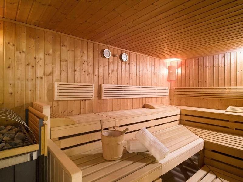 Holzsauna mit hellen Holzliegen, Thermometern an der Wand und einem Holzeimer mit Kelle.