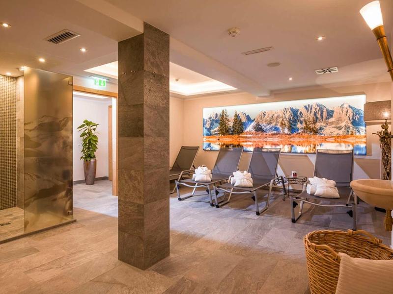 Heller Spa-Raum mit Liegen, Pflanze, Dusche, Wandbild mit Herbstlandschaft und warmem Licht.