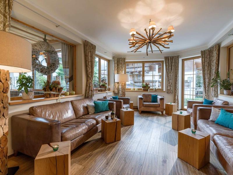 Gemütliches Wohnzimmer mit braunem Ledersofa, Holzmöbeln, großen Fenstern und warmem Licht.