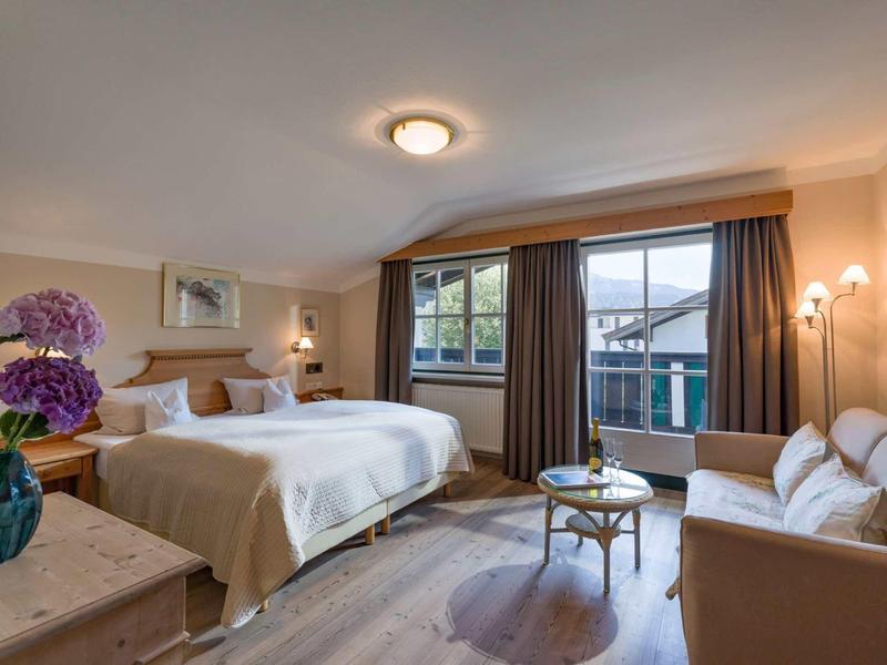 Helles Schlafzimmer mit großem Bett, Sofa, Blumen und Fenster mit Blick auf Berge.