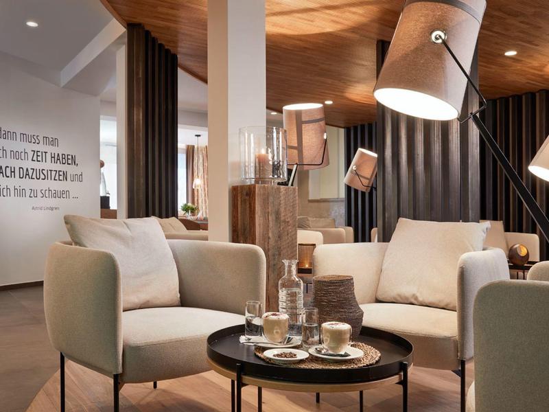 Gemütliches Wohnzimmer mit zwei Sesseln, Sofa, runden Tisch, Lampen und Holzwanddecke.