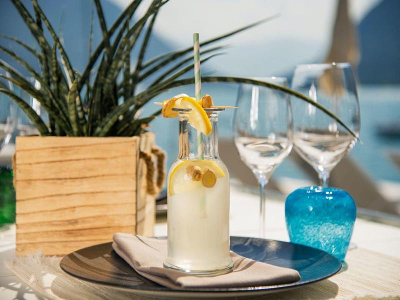 Tropischer Cocktail mit Ananasscheibe auf Tisch mit Pflanzen, Gläsern und blauem Dekor, sonnig.