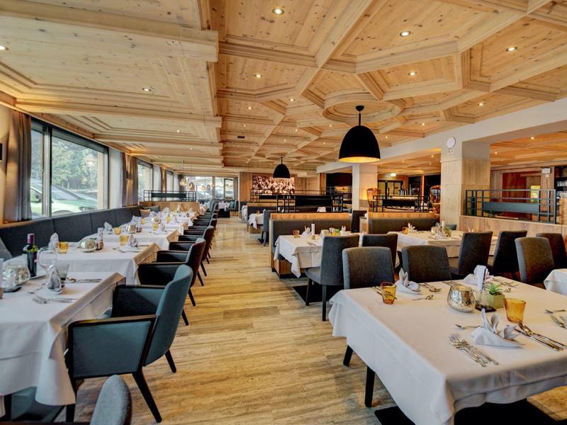 Großes Restaurant mit gedeckten Tischen, schwarzen Stühlen, Holzboden und hellen Holzbalkendecken.