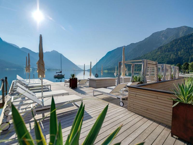 Terrasse mit Holzbohlen, weißen Liegen und Bergen unter blauem Himmel im Hintergrund.