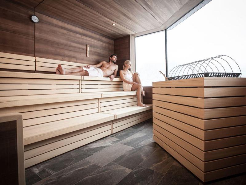 Moderne Sauna mit Holzverkleidung, dreistufigen Bänken und großen Fenstern, zwei Personen entspannen.