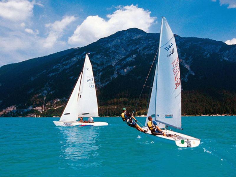 Zwei weiße Segelboote auf türkisblauem Wasser vor bewachsenen Bergen unter blauem Himmel.
