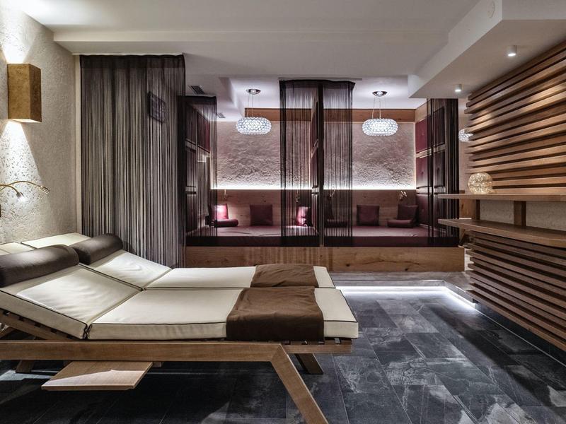 Moderner Wellnessraum mit Liegestühlen, dunklen Vorhängen, Holzpaneelen und gedämpfter Beleuchtung.