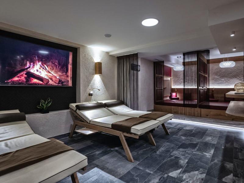 Moderne Spa-Lounge mit Liegestühlen, Kaminprojektor und gedämpfter Beleuchtung für Entspannung.