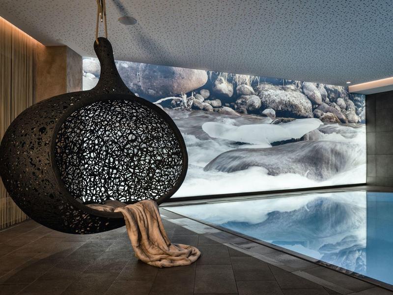 Moderner Innenpool mit hängendem Korbsessel und großem Wandbild in neutralen Farbtönen.