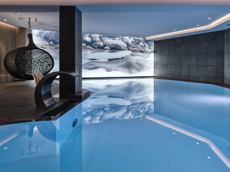 Moderner Innenpool mit klar blauem Wasser, grauen Wänden und großem Landschaftsbild an der Wand.