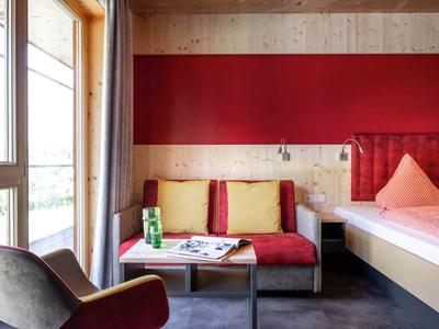 Modern hotel room with red accent sofa, cushions, and a window with curtain.