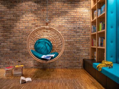 Gemütliche Leseecke mit Hängesessel, Bücherregal und blauer Sitzbank vor Ziegelwand.