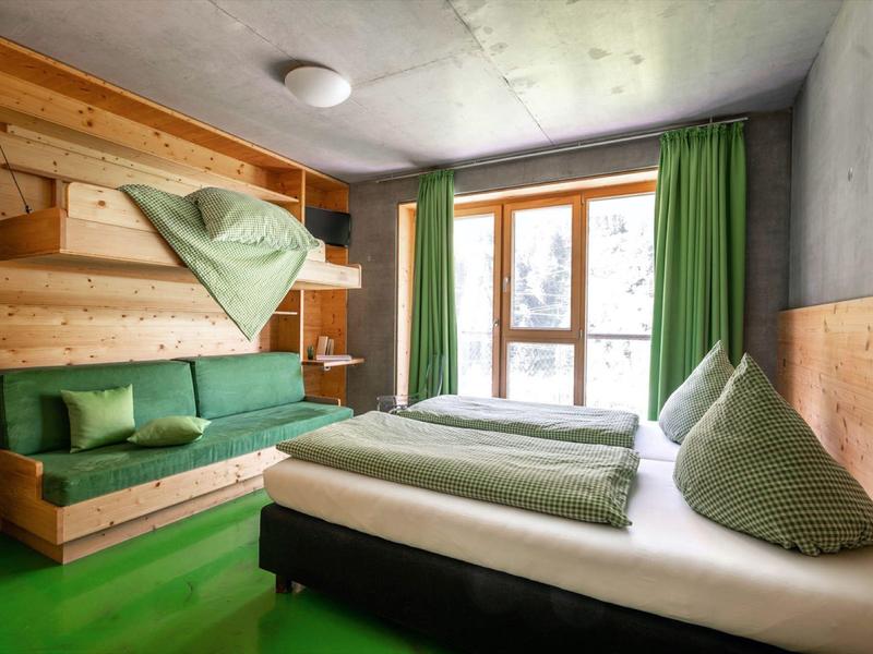 Cozy hotel room with wooden furniture, green sofa, green curtains, and a large window.