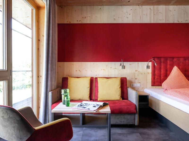 Modern hotel room with red accent sofa, cushions, and a window with curtain.