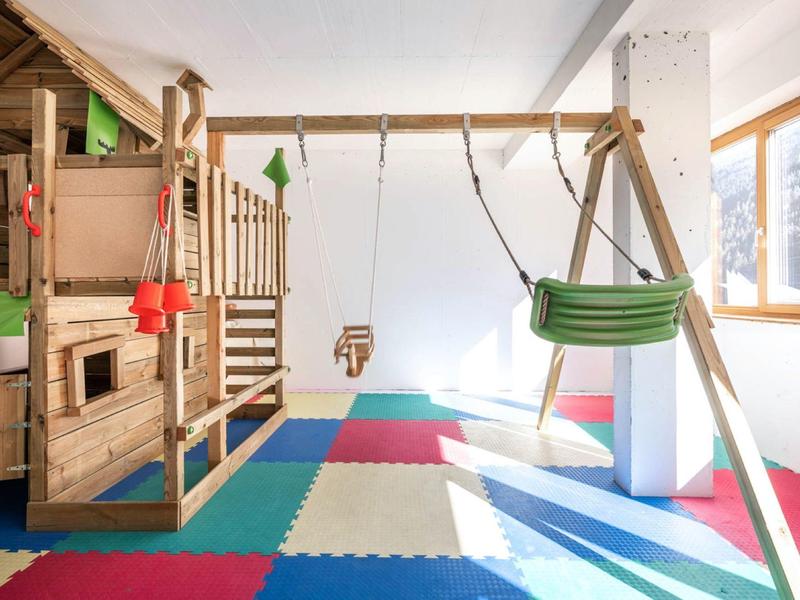 Bright playroom with wooden house, swings, and colorful foam flooring.
