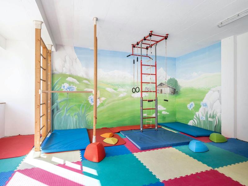 Colorful indoor play area with climbing equipment and a nature-themed mural.