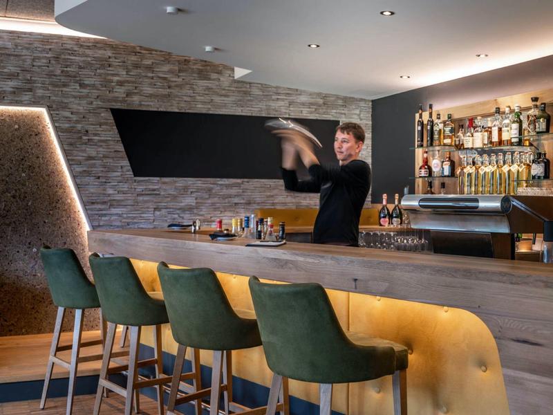 Bartender preparing drinks in a modern hotel bar with green bar stools.