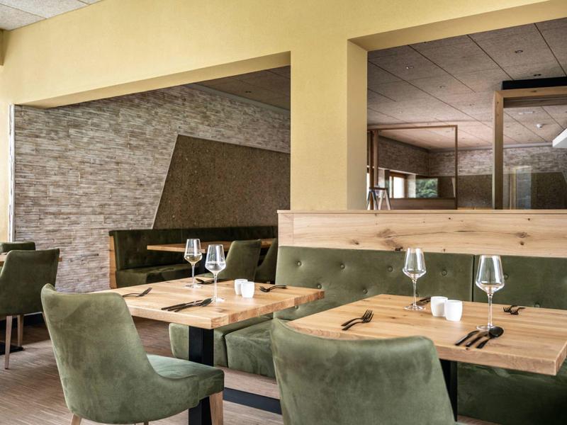Cozy dining area with green chairs, wooden tables, and stone wall in modern design.