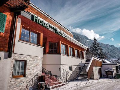 Holzhaus-Hotel im Bergstil mit Schnee, Treppe, grünen Fensterläden und blauem Himmel im Hintergrund.