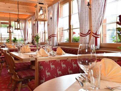 Gemütlicher Restaurantbereich mit rustikaler Holzdecke, Tischgedecken und roten Sitzbänken.