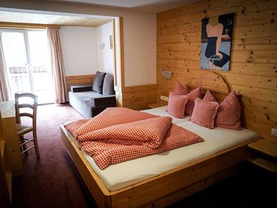 Gemütliches Schlafzimmer mit Holzwand, Doppelbett, rosa Bettwäsche und Blick auf Balkon und Sitzbereich.