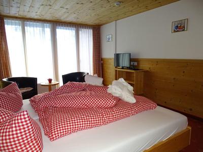 Gemütliches Schlafzimmer mit zwei Betten, rot-weiß karierten Decken und zwei Sesseln am Fenster.