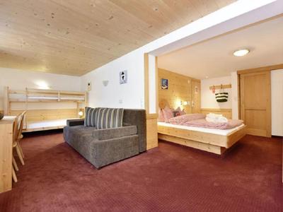 Geräumiges Zimmer mit zweigeteiltem Schlafbereich, Holzmöbeln, Teppichboden und Deckenbeleuchtung.