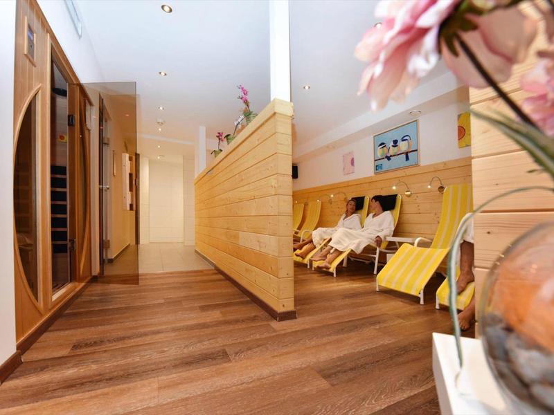 Moderner Flur mit Holzverkleidung, Holzboden und Sitzbereich mit gelben Liegen und Blumendeko.