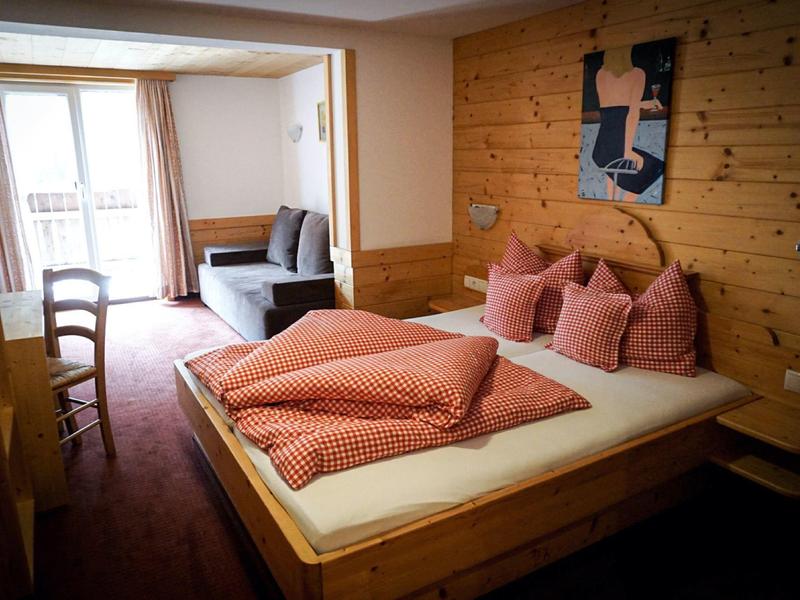 Gemütliches Schlafzimmer mit Holzwand, Doppelbett, rosa Bettwäsche und Blick auf Balkon und Sitzbereich.