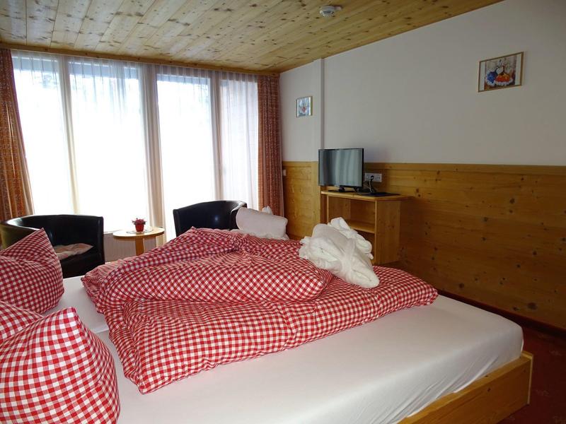 Gemütliches Schlafzimmer mit zwei Betten, rot-weiß karierten Decken und zwei Sesseln am Fenster.