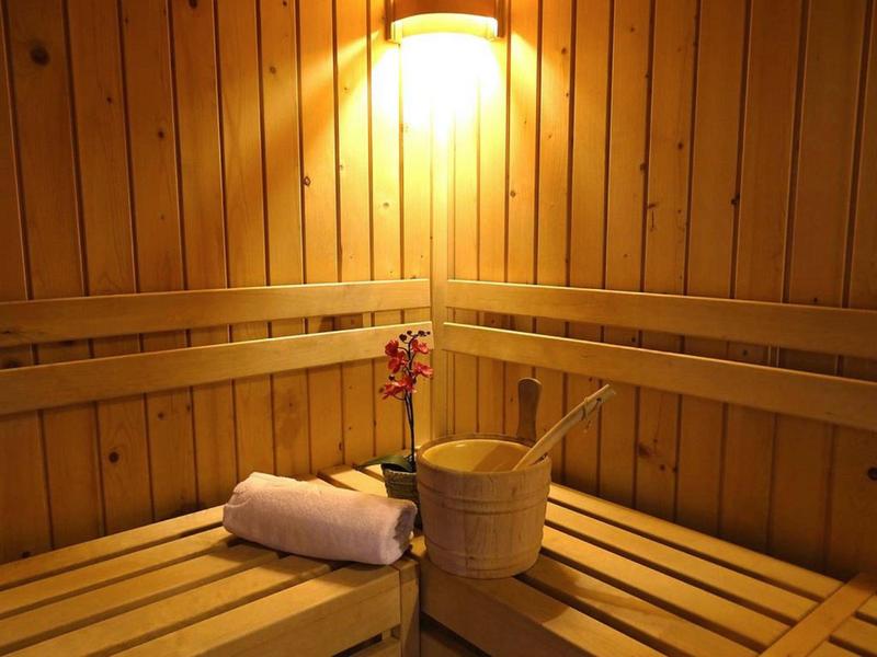 Holzsauna mit Sitzbänken, Handtuch, Blumendekoration und Holzeimer unter warmem Licht.