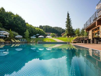 Piscina con lettini e ombrelloni accanto a edificio in legno, circondata da colline verdi.
