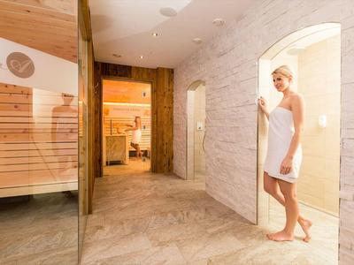 Frau mit Handtuch im weißen Saunabereich mit hellem Holz und Fliesenboden.