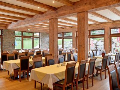 Grote eetzaal met houten balken, tafels en stoelen, licht en uitnodigend.