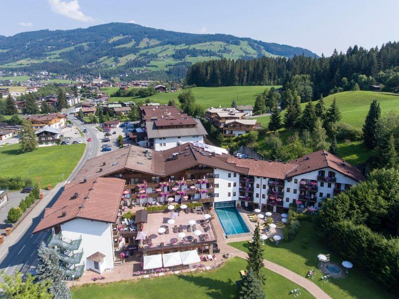 Großes Hotel im Tal mit Pool, Terrassen und umliegenden grünen Wiesen und Bergen.