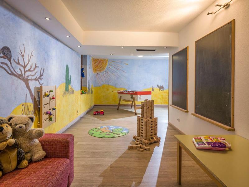 Kindgerechter Spielraum mit bunten Wandbildern, Holzspielzeug, zwei Plüschigeln und Schultafeln an der Wand.