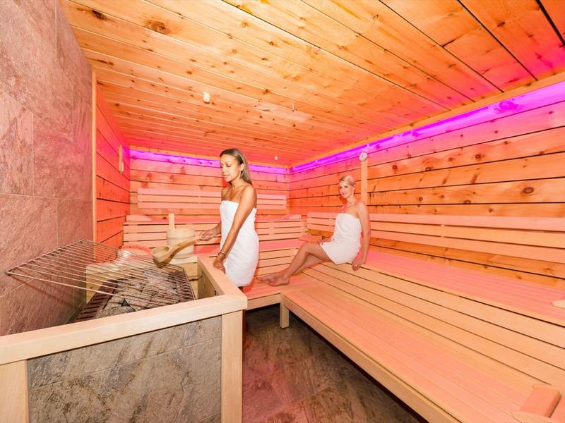 Zwei Frauen entspannen in einer Holzsauna mit rosa LED-Beleuchtung an den Wänden.