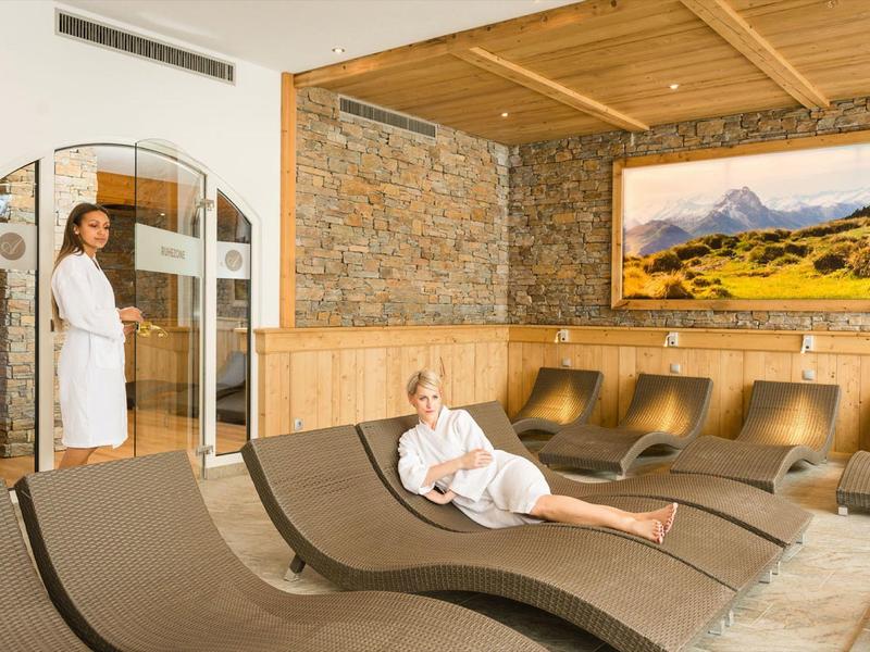 Entspannte Frau im Bademantel auf Wellenliege im Saunabereich mit Steinwand und Naturbild.